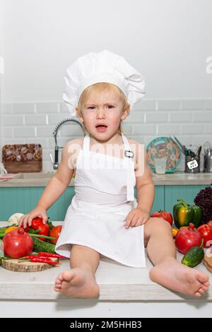 A cute little boy in a chef's costume cooks food with emotions. High quality photo Stock Photo