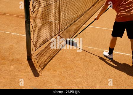 Maintenance of the tennis court. Brushing lines on a clay tennis court. Grid and shadow. Legs and hands of a teenager. Stock Photo