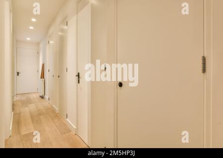 a long hallway with white walls and wood flooring on either side by side, there is an open door leading to another room Stock Photo