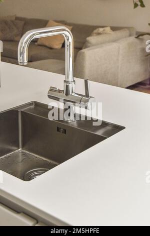 a kitchen sink with water running from the fauced tap in it's right hand held over the sink Stock Photo
