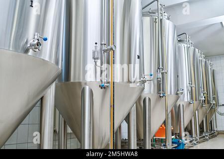 Stainless steel tanks for brewing drinks standing in a row in storage room of factory Stock Photo