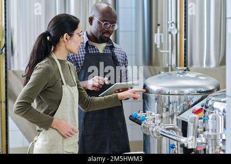 Couple of engineers examining the condition of steel barrel for brewing together using digital tablet Stock Photo