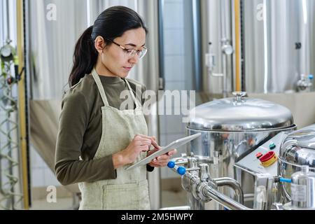 Serious young engineer concentrating on her online work on digital tablet, she controlling the work of equipment in workshop Stock Photo