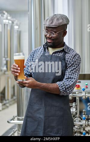 Young African American engineer holding glass of beer in his hands tasting it after brewing Stock Photo
