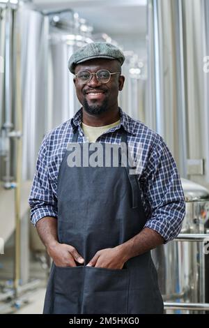 Portrait of African American man in uniform smiling at camera, he working in brewery factory Stock Photo