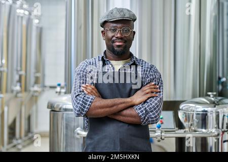 Portrait of African American worker standing in workshop of brewery with his arms crossed and looking at camera Stock Photo