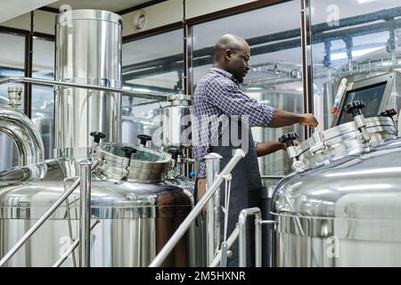 African American man using special equipment to brew beer in workshop Stock Photo