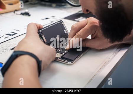 In the electronics repair shop, the master repairs, cleans, controls, arranges the smartphone. Uses equipment and tools for work. Workplace top view, Stock Photo