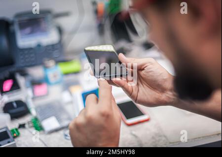 In the electronics repair shop, the master repairs, cleans, controls, arranges the smartphone. Uses equipment and tools for work. Workplace top view, Stock Photo