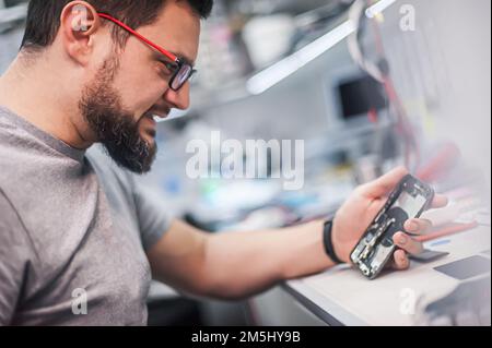 In the electronics repair shop, the master repairs, cleans, controls, arranges the smartphone. Uses equipment and tools for work. Workplace top view, Stock Photo