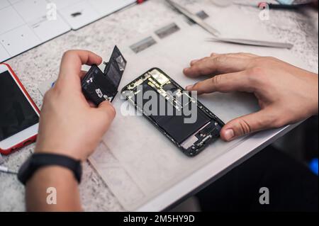 In the electronics repair shop, the master repairs, cleans, controls, arranges the smartphone. Uses equipment and tools for work. Workplace top view, Stock Photo