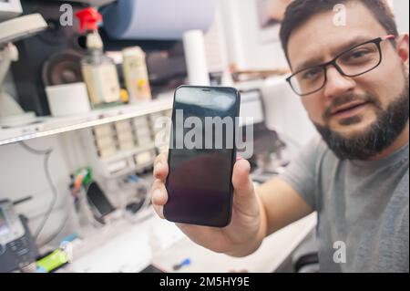 In the electronics repair shop, the master repairs, cleans, controls, arranges the smartphone. Uses equipment and tools for work. Workplace top view, Stock Photo