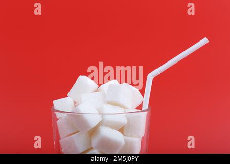Glass with straw full of sugar cubes isolated on red background. A metaphor for the fact that drinks often contain a lot of sugar Stock Photo