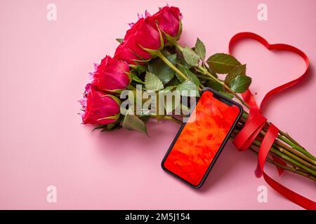 Pink roses bouquet with hart shaped bow and mobile phone with copy space screen Stock Photo