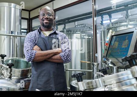 Portrait of African American engineer smiling at camera standing with his arms crossed, he working at modern brewery Stock Photo