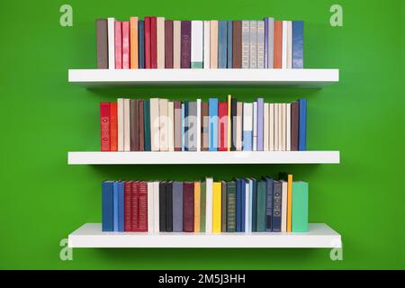 neat rows of books on white shelves against a green wall Stock Photo