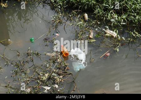 A small waterway filled with rubbish like Plastic waste and polythene bags and weed plants in Sri Lanka Stock Photo