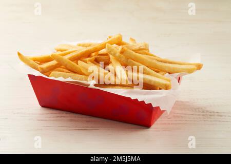 One serving of French fries in a cardboard container on wooden table Stock Photo