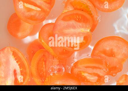 Close-up view of the red tomato slices in water background. Texture of cooling vegeteble drink with macro bubbles on the glass wall. Flat design. Stock Photo