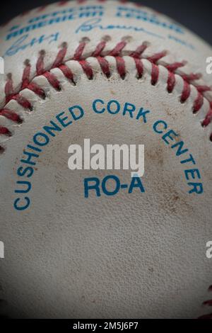 A close-up capture of a game used baseball with red stitching and blue printing stating the ball has a "cushioned cork center". Stock Photo