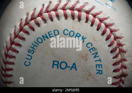 A landscape close-up capture of a game used baseball with red stitching and blue printing stating the ball has a "cushioned cork center". Stock Photo