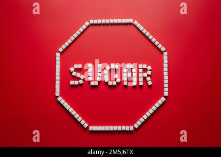 octagonal frame in the form of a stop sign made of sugar cubes with red background and word sugar inside. stop eating refined sugar flat lay concept Stock Photo