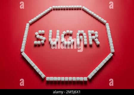 octagonal frame in the form of a stop sign made of sugar cubes with red background and word sugar inside. stop eating refined sugar concept Stock Photo