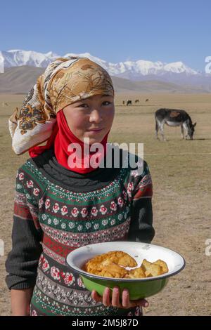 Achik Tash, Kyrgyzstan - 08 30 2018 : Portrait of young Kyrgyz girl showing traditional hospitality by offering doughnuts in the rural countryside Stock Photo