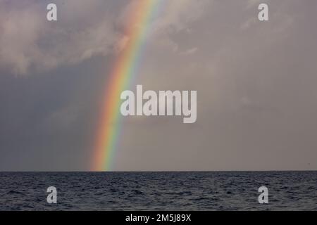A bright rainbow, caused by sunlight refracting through water droplets, appears over the South Pacific Ocean during the monsoon season. Stock Photo