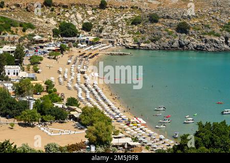 Lindos, Rhodes, Greece - May 2022: Aerial view of rows of sun umbrellas on the beach near the town Stock Photo
