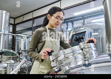 Female young engineer working on equipment to control the process of brewing Stock Photo