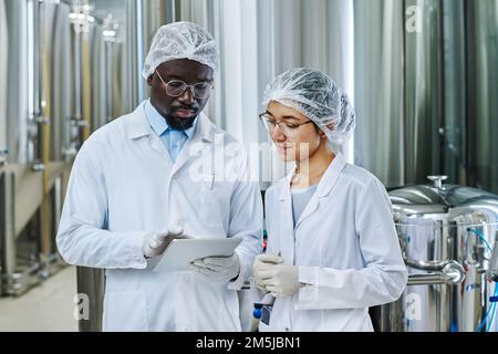 Multiethnic couple of engineers working together with digital tablet while working at brewery Stock Photo