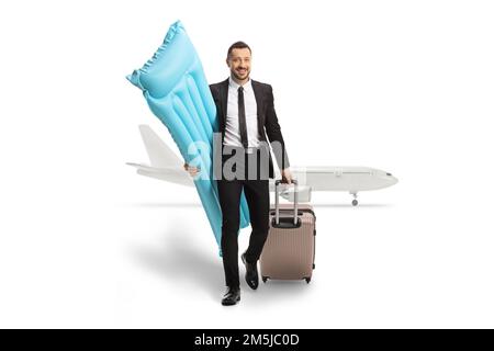Businessman carrying a floating mattress and pullung a suitcase in front of an airplane isolated on white background Stock Photo