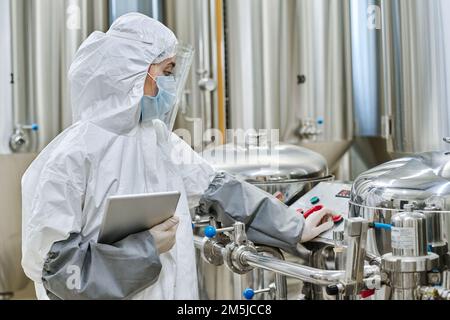 Engineer in protective workwear controlling machinery with panel at chemical factory Stock Photo