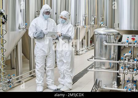 Chemists in protective workwear using tablet pc during their teamwork at chemical factory Stock Photo
