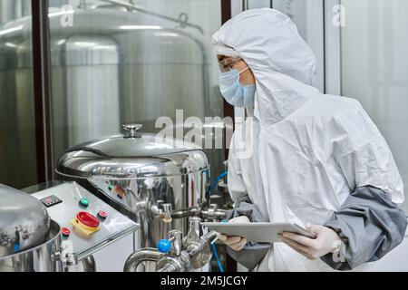 Worker in protective costume using tablet pc to check the work of equipment in workshop Stock Photo