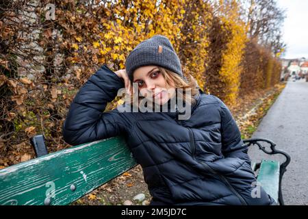 Young girl is sitting on a green bench in the garden of Schloss Belvedere in Vienna. Portrait of a beautiful girl with a background of yellow and brow Stock Photo