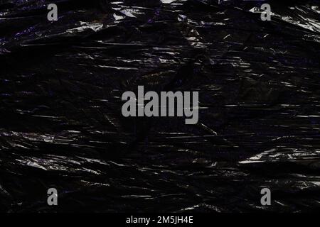 Black color plastic wrap background. Dark crumpled wrinkled plastic cellophane. Reflecting blue light and shadow on creases and folds in plastic Stock Photo