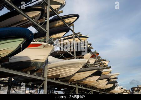 View from below of the hulls of motorboats racked one above another on two levels in a dry rack boat storage facility against blue sky. Stock Photo