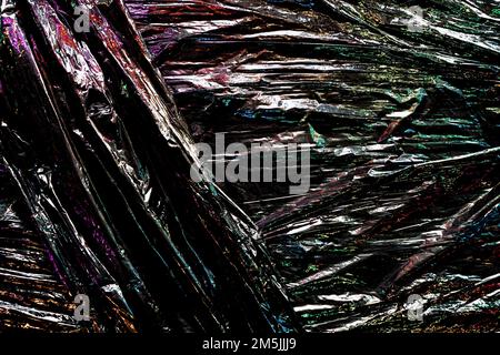 Black color plastic wrap background. Dark crumpled wrinkled plastic cellophane. Reflecting colorful iridescent light and shadow on creases and folds Stock Photo
