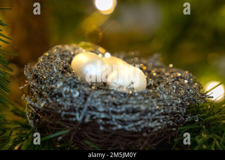 Eggs in a birds nest Christmas ornament in an artificial Christmas tree with Christmas lights in background Stock Photo
