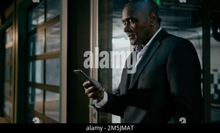 Serious focused businessman holding mobile phone chatting on internet browsing social network mature african man communicate with business client Stock Photo