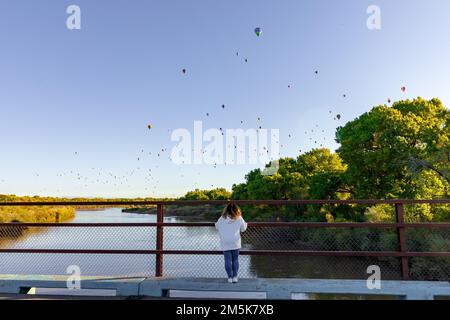 A lady in front of a metallic fence watching hot air balloons over Albuquerque, New Mexico, USA Stock Photo