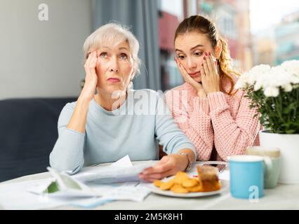 Worried elderly woman with adult daughter checking utility bills Stock Photo