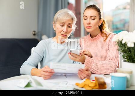 Elderly woman with adult daughter using smartphone and checking utility bills Stock Photo