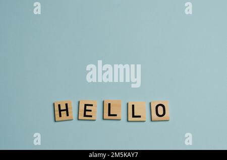 Hello salutation or greeting word to welcome someone or initiate a conversation. Design with letters cut out in wood speech bubble over blue backgroun Stock Photo