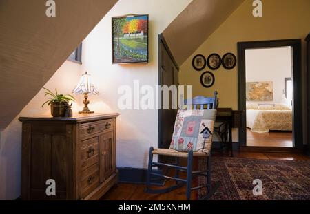 Old wooden antique dresser and blue painted rocking chair with weaved seat on upstairs hallway inside reconstructed 1840s log home. Stock Photo