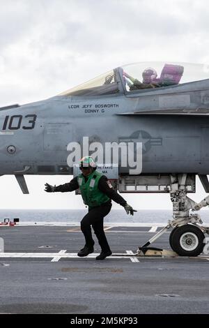 Aviation Boatswain's Mate (Equipment) 3rd Class Lacarsha Mitchell, from Chicago, assigned to USS Gerald R. Ford's (CVN 78) air department, sweeps the deck as an F/A-18E Super Hornet attached to the 'Ragin' Bulls' of Strike Fighter Squadron (VFA) 37 prepares to launch from the flight deck during flight operations, March 23, 2022. Ford is underway in the Atlantic Ocean conducting flight deck certification and air wing carrier qualifications as part of the ship’s tailored basic phase prior operational deployment. Stock Photo