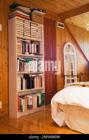 King size bed and bookcase in guest bedroom on upstairs floor inside old 1920s cottage style home. Stock Photo