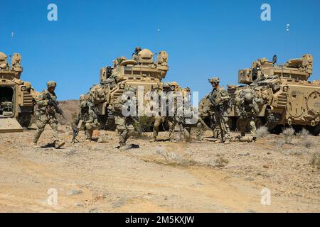 U.S. Army Soldiers assigned to 3rd Battalion, 8th Cavalry Regiment, 3rd Armored Brigade Combat Team, 1st Cavalry Division exits their M2 Bradley Fighting Vehicle in order to conduct dismount operations during Decisive Action Rotation 22-05 at the National Training Center, Fort Irwin, Calif., Mar. 23, 2022 Stock Photo